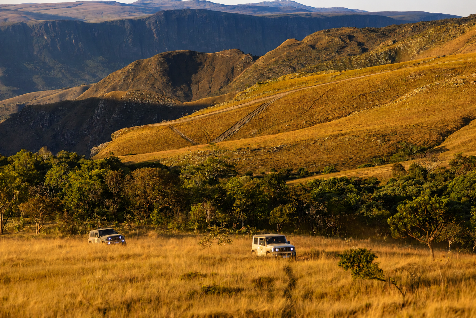 Comboio 4x4 atravessando dunas ao pôr do sol